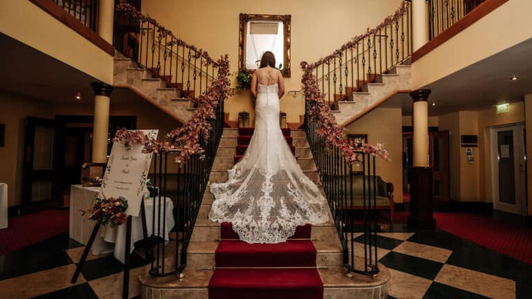 Bride in a lace wedding dress standing on the Roganstown Hotel staircase