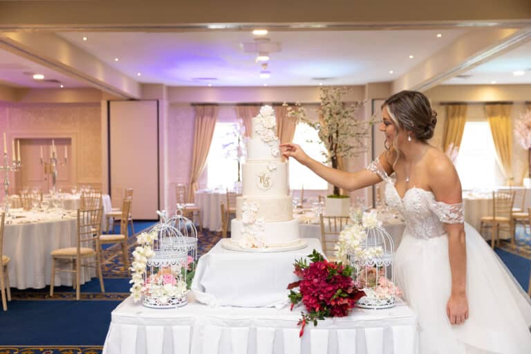 Bride admiring a five-tier white floral wedding cake with birdcage decorations in the function room at Roganstown Hotel