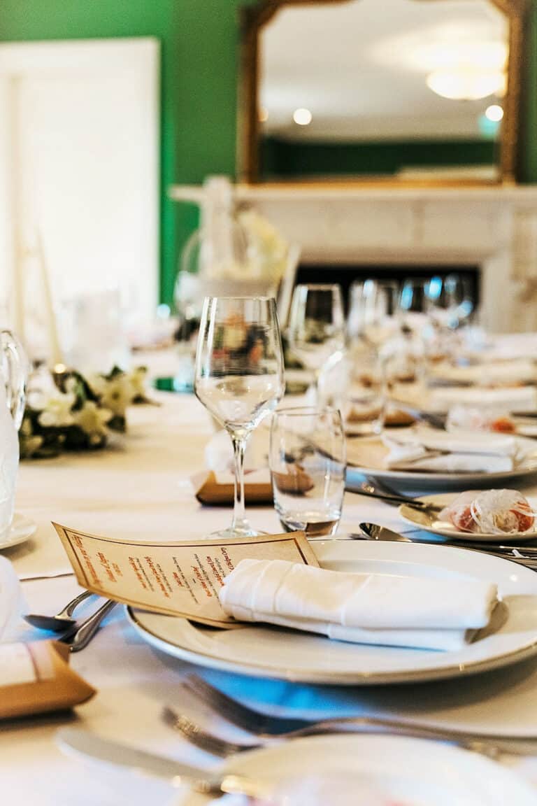 Close-up of a wedding place setting with menu card, glassware and folded napkin in a green-walled dining room at Roganstown