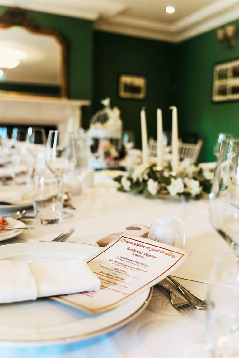 Wedding table set with a personalised menu, glassware and candle centrepiece in a green-walled private dining room at Roganstown