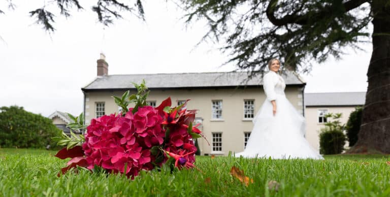 Pink hydrangea and fuchsia bouquet resting on the grass with a bride in a white gown and faux fur wrap at Roganstown Hotel