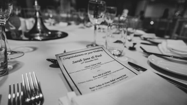 Black and white close-up of a personalised wedding menu card on a set dining table in the Roganstown Hotel function room